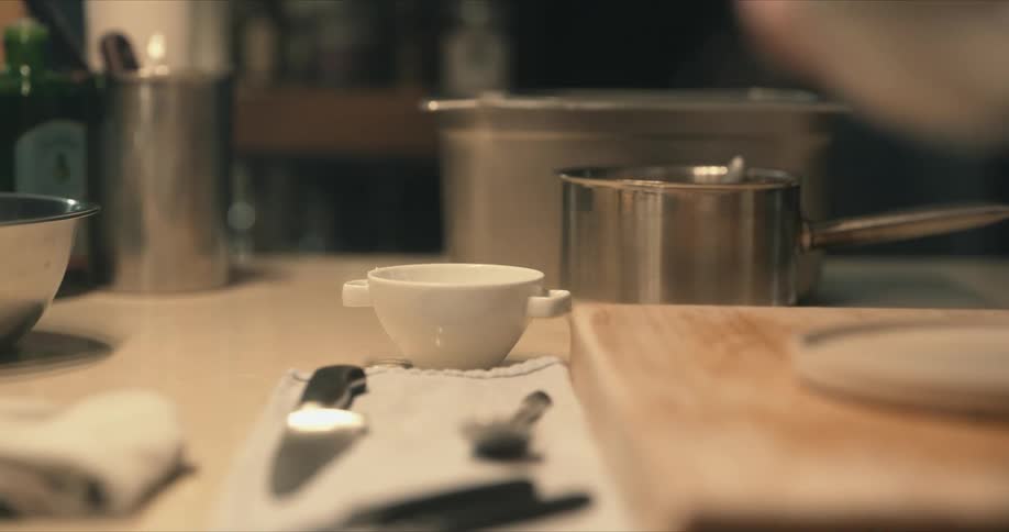 A man picks up flour from a small bowl and sifts it near his cutting board