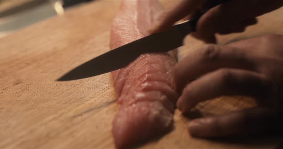A person is slicing a fish fillet with a knife on a cutting board