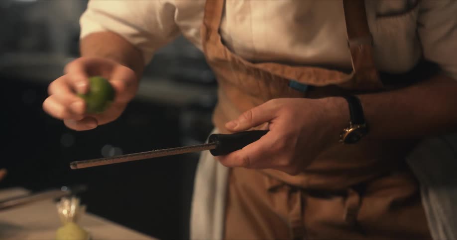 A cook is grating lime on sliced fish on a black plate sitting on a cutting board