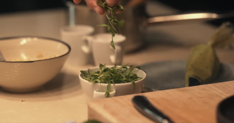 A chef takes herbs from a cup on a table near a plate of food