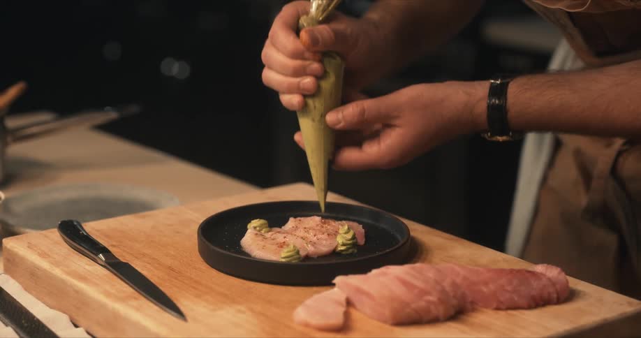A chef garnishes sliced fish with wasabi