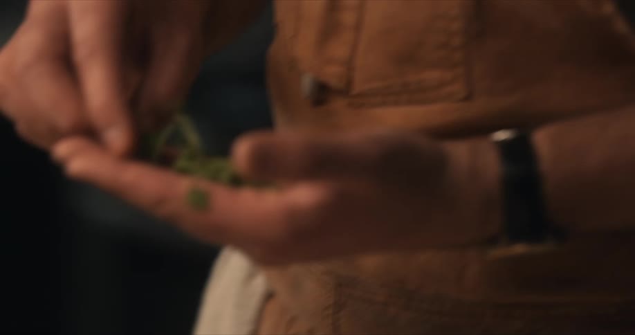 A chef is standing over a table with herbs in his hand