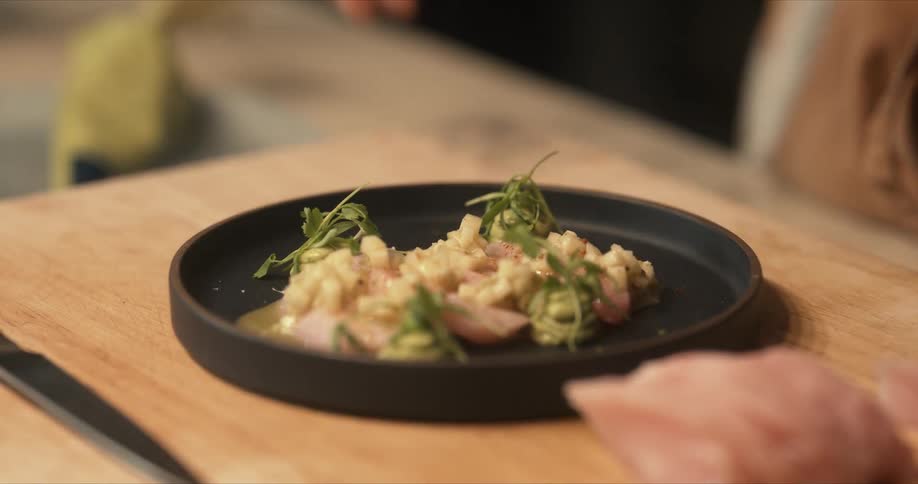 Chef garnishes food on a small dark dish at home