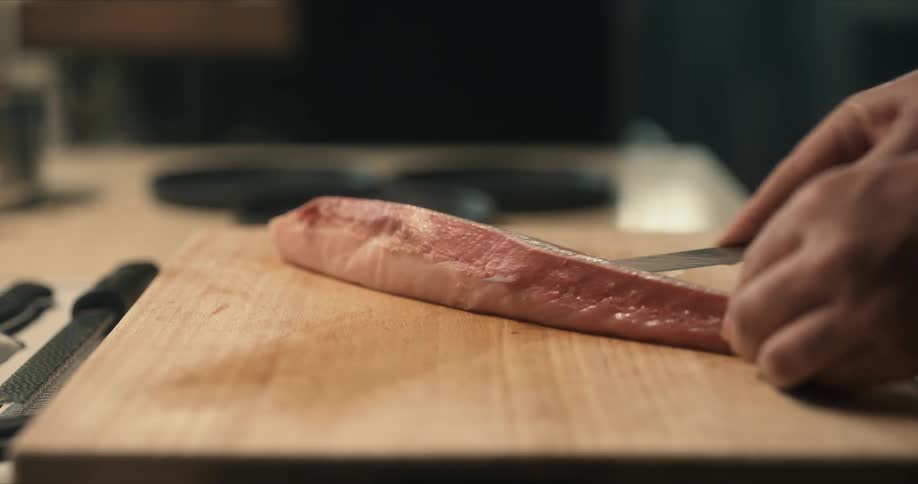 A person uses a knife to slice raw meat on a wooden cutting board