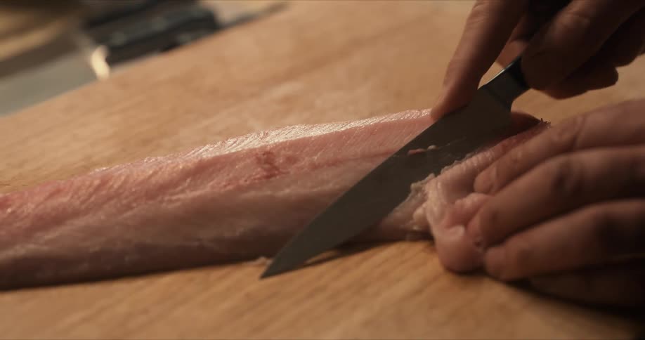 A person uses a knife to slice raw fish on a wooden cutting board