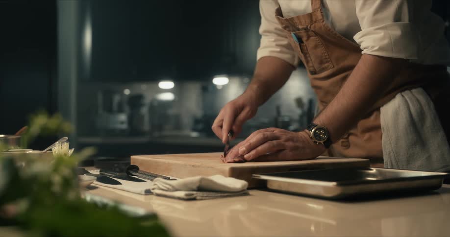 A man uses a knife to cut a piece of raw meat in a large kitchen