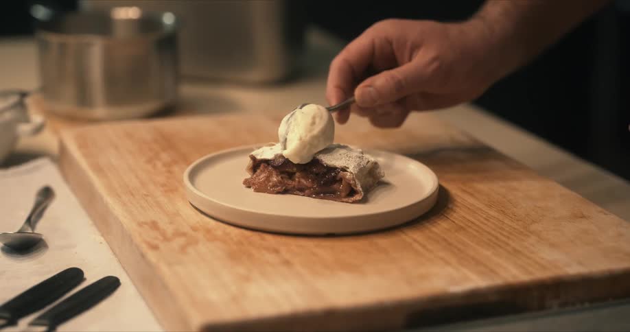 A man prepares a dessert by adding whip cream to the top