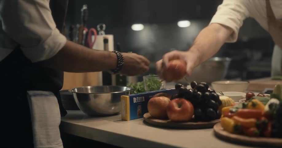 Two male chefs using fruit and herbs while cooking at kitchen island