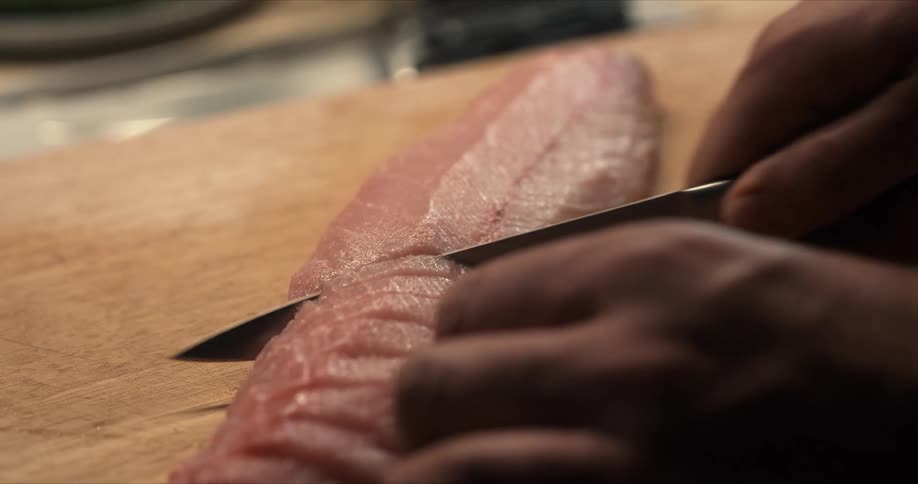 A person is cutting raw fish into slices