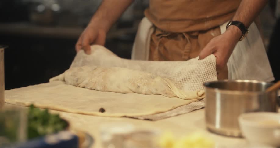 A chef is in a kitchen rolling a stromboli and brushing the dough with a pastry brush