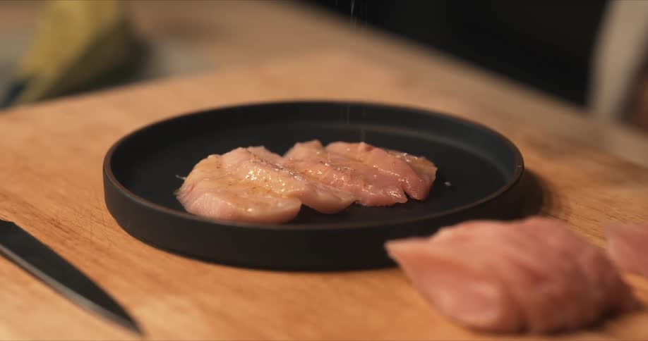 A chef seasons raw fish on a plate