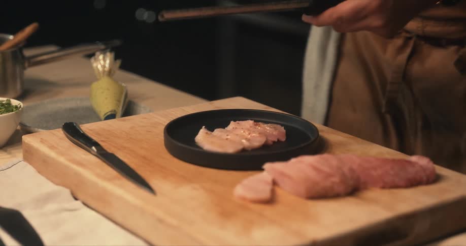 A person adds some seasoning to raw fish on a cooking plate