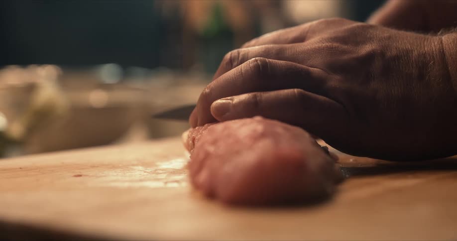 A man uses a knife to slice raw fish on a wooden cutting board