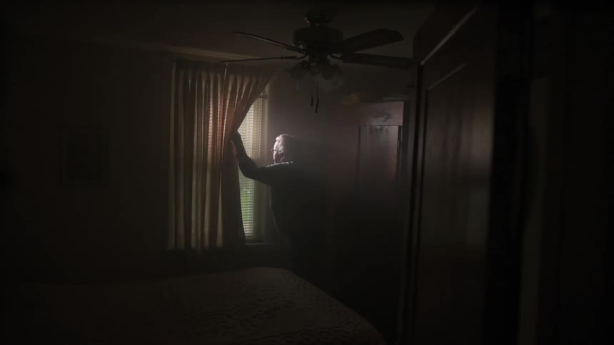 A person peaks out of the blinds of his dark home