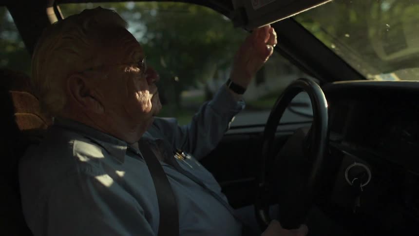 An elderly man drives a car in a residential area