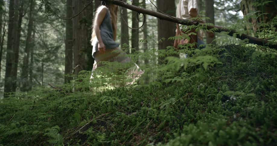 Two teenage girls are walking in the woods as the sun shines through the trees