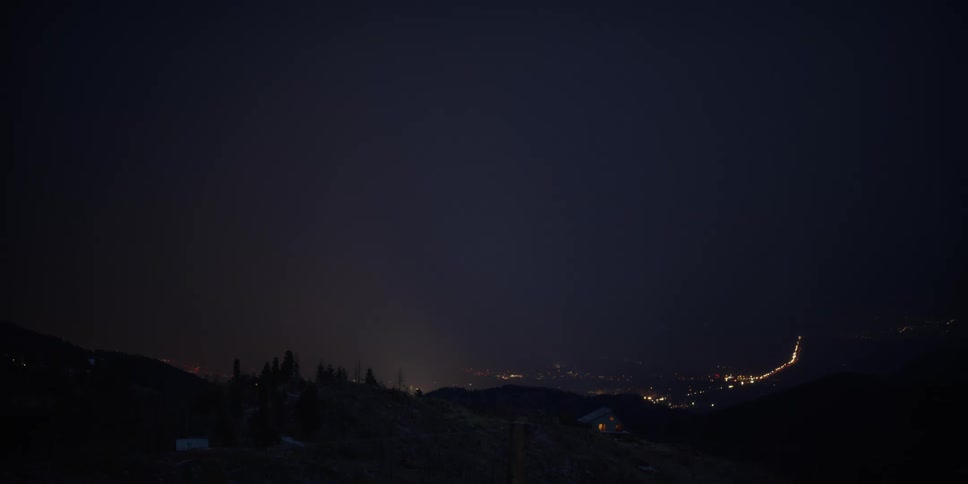 Lights are on in a house on a hill and a valley below is lit up as lightning flashes in the night sky above