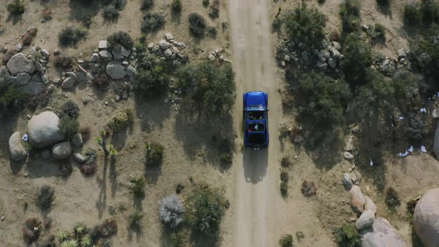 A vehicle travels along a dirt road through a shrubland during the day