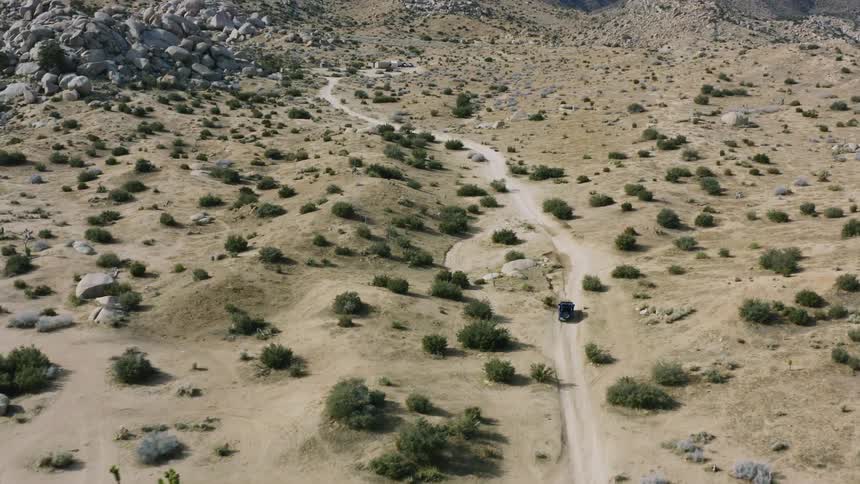 A vehicle travels along a dirt road through a hilly countryside during the day