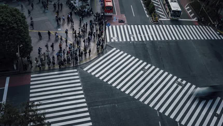 Many people are crossing the street at a busy intersection and traffic is moving on the street