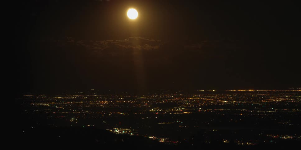 The moon rises into the sky above the city