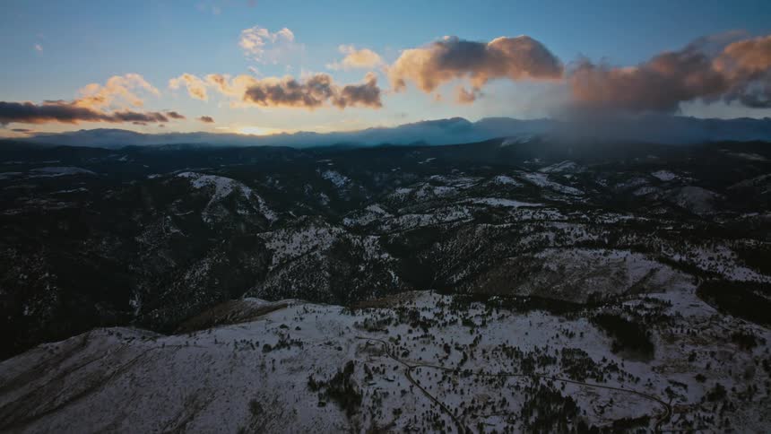 Clouds move over snow covered forested mountains and there are mountains in the distance