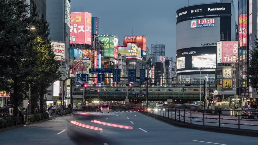 Traffic travels along a wide street in a metropolis as the sky begins to darken