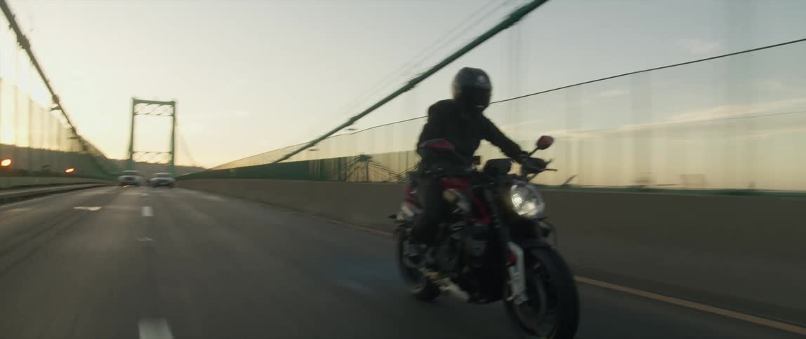 Motorcycle travels over a bridge as two cars approach in the distance