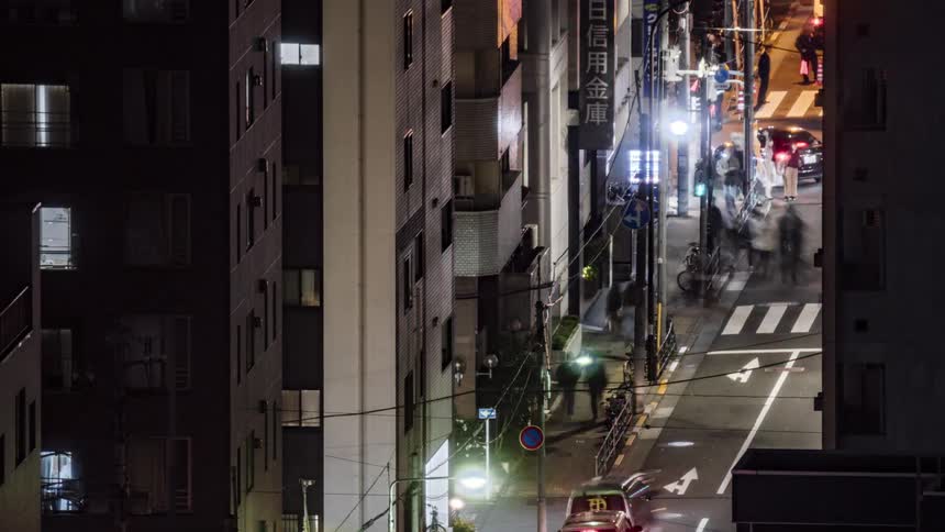 Vehicles and crowds of pedestrians travel along a street in a metropolis at night