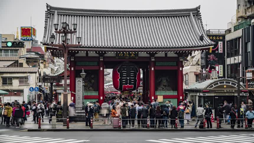 Large crowd of pedestrians move around shrine as traffic passes on nearby road