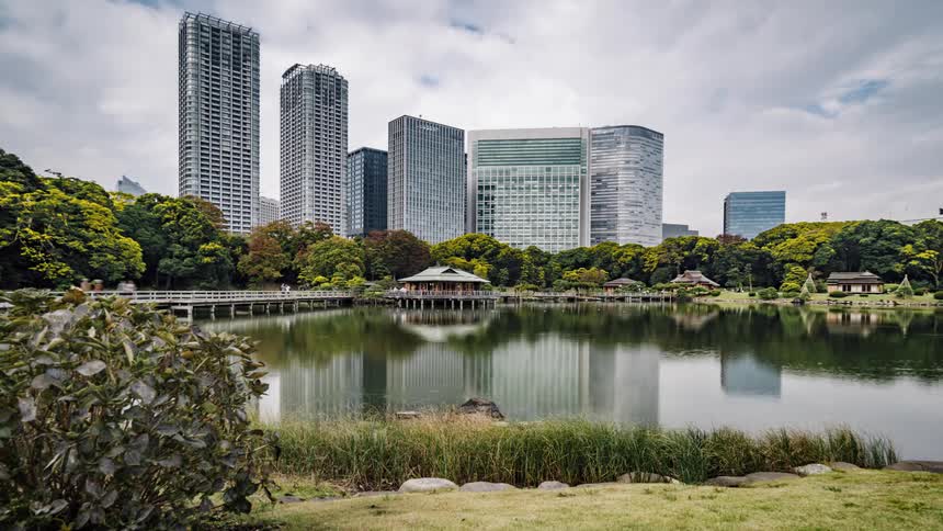 People walk across the bridge over the water in hamarikyu gardens