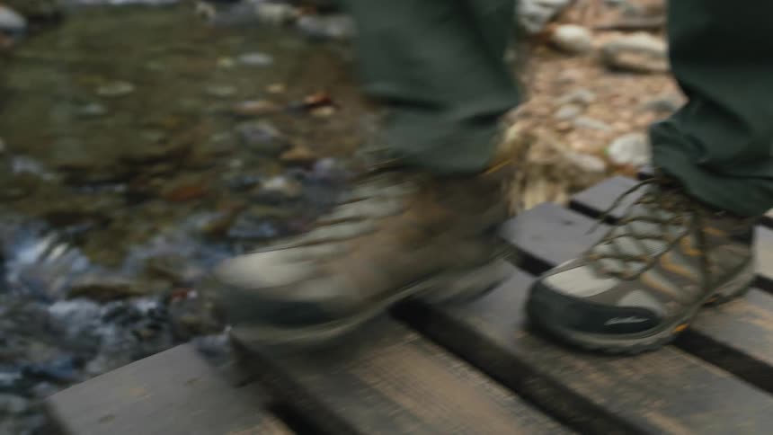 A man is walking on a footbridge across a creek