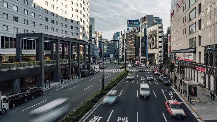 Traffic travels along a wide road in a metropolis during the day