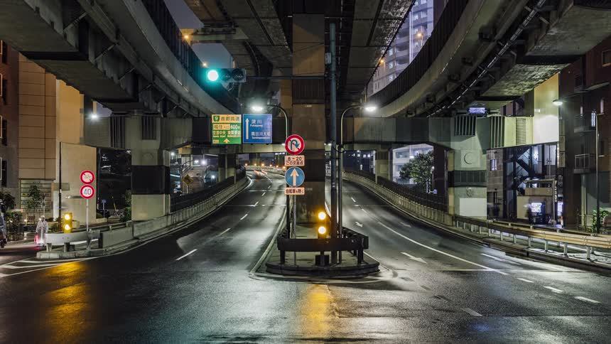 Traffic moves on a busy highway in and out of downtown as lights reflect on the wet road at night and people walk on the sidewalks