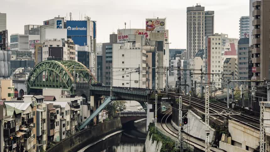 Trains travel on the tracks on a bridge over a river in the city
