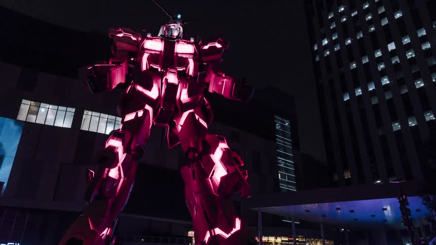 Lights are flashing on a giant robot standing outside near tall buildings at night