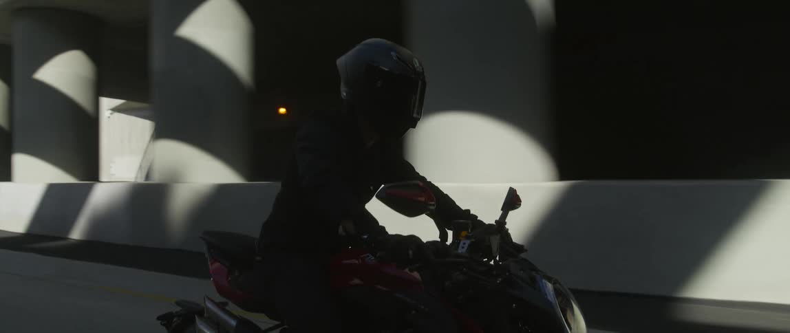 A cyclist wearing a black helmet is riding a motorcycle through a dark underpass