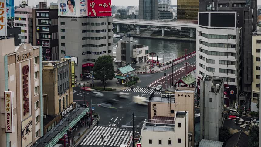 Automobiles travel on a busy downtown intersection around tall buildings as traffic moves on a bridge over water