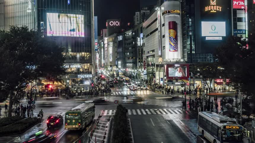 Traffic and pedestrians cross the city street at a downtown intersection at night
