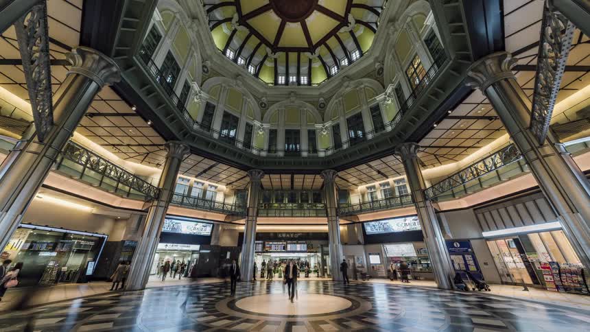 People are busy walking in a public shopping mall and messages are flashing on screens above the shops