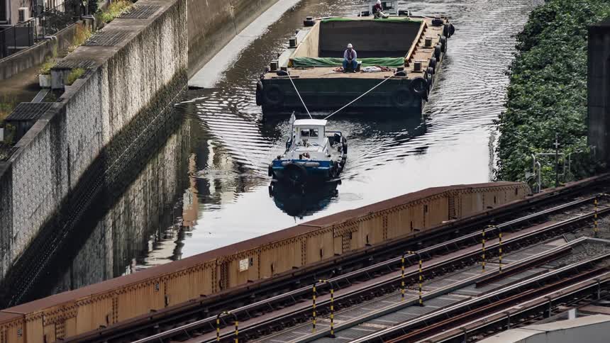 Small tugboat towing a barge on a channel through the city under a bridge