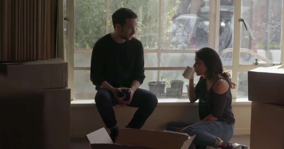 A man and woman converse while sipping coffee in a living room
