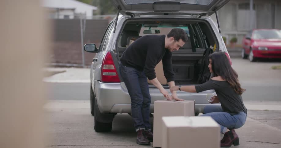 A man and woman tape boxes by a car