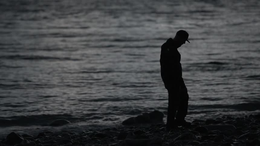 A man walks along the rocks of a shore at night