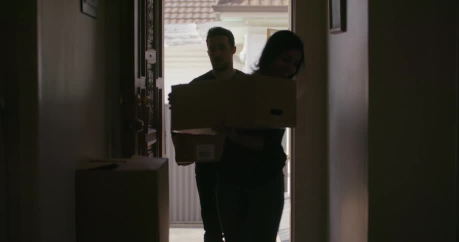 A man and woman carry boxes into a house
