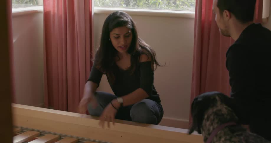 Woman picks up a piece of a bed and hands it to a man with a dog nearby