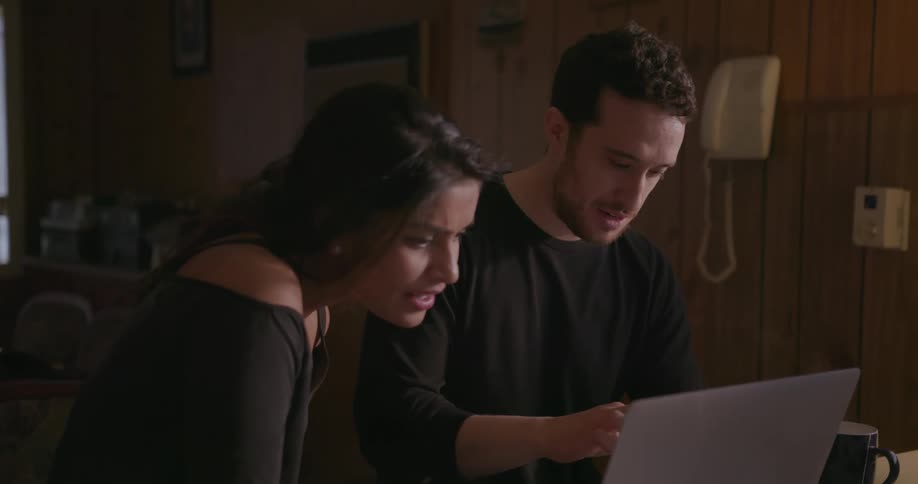 A man and woman are discussing things on a laptop as they sit at a kitchen counter