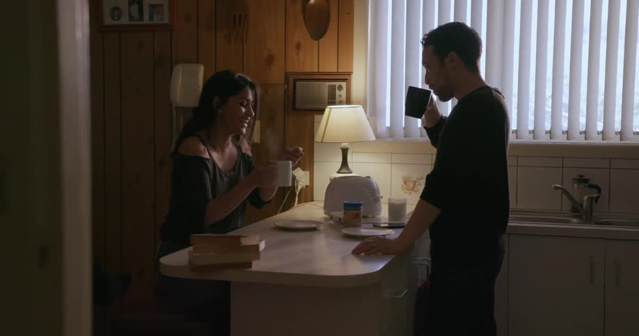 Couple at a kitchen counter drinking coffee and agreeing on something by clicking cups