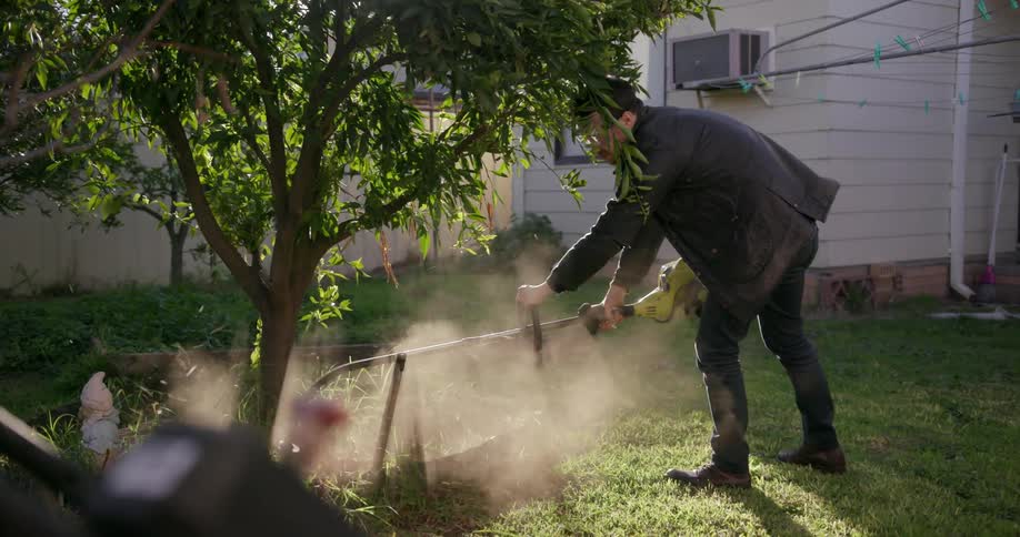 Man uses a trimmer to cut grass in a backyard