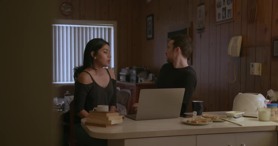 A man and woman are sitting at the kitchen counter using the laptop